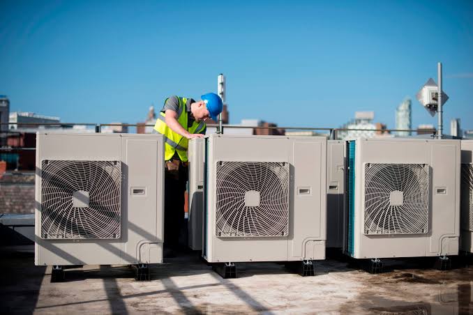 Technician servicing rooftop commercial AC condenser units on a Dallas building