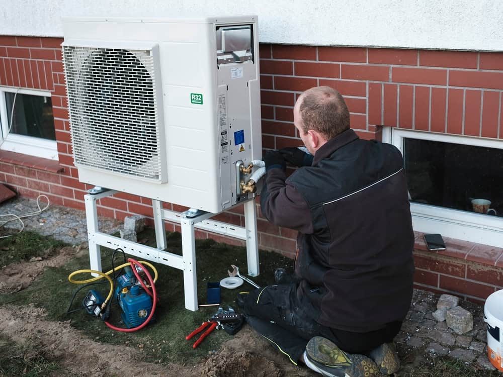 Technician installing a heat pump outdoor unit with refrigerant gauges on a Dallas home's exterior wall